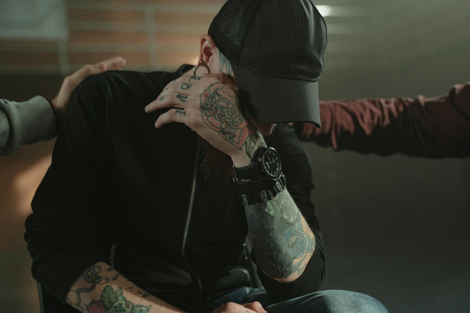 A comforting moment showing a tattooed person being consoled by friends indoors.