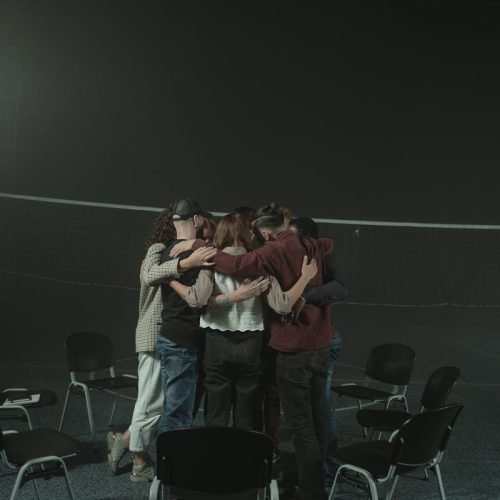 A small group of diverse adults embracing in a supportive circle indoors, symbolizing unity and support.